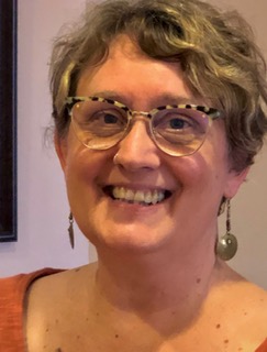 Smiling portrait of Mirren McConnell at River Ridge Chiropractic in Asheville, NC, wearing glasses and drop earrings.